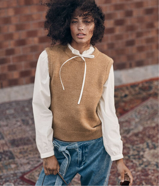 Woman wearing a white blouse with a tied high neck, layered under a brown wool sweater vest