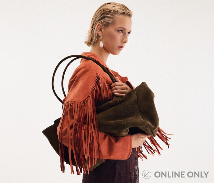 Young woman wearing an orange faux suede fringed jacket and holding a large brown faux suede tote bag