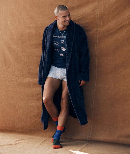 Homme debout en peignoir bleu marine, sous-vêtement blanc et chaussettes colorées.