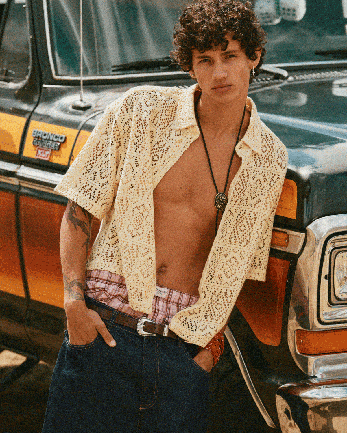A young man at the beach wearing an open crochet shirt and loose capri jeans