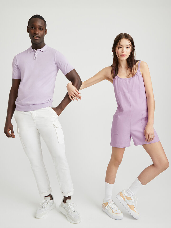 Homme vêtu d'un t-shirt lilas et d'un pantalon blanc et femme vêtue d'une combinaison lilas