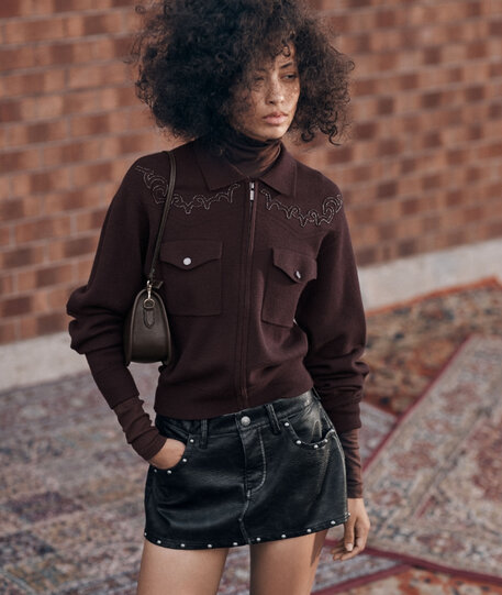 Woman standing wearing a black leather mini-skirt with stud accents