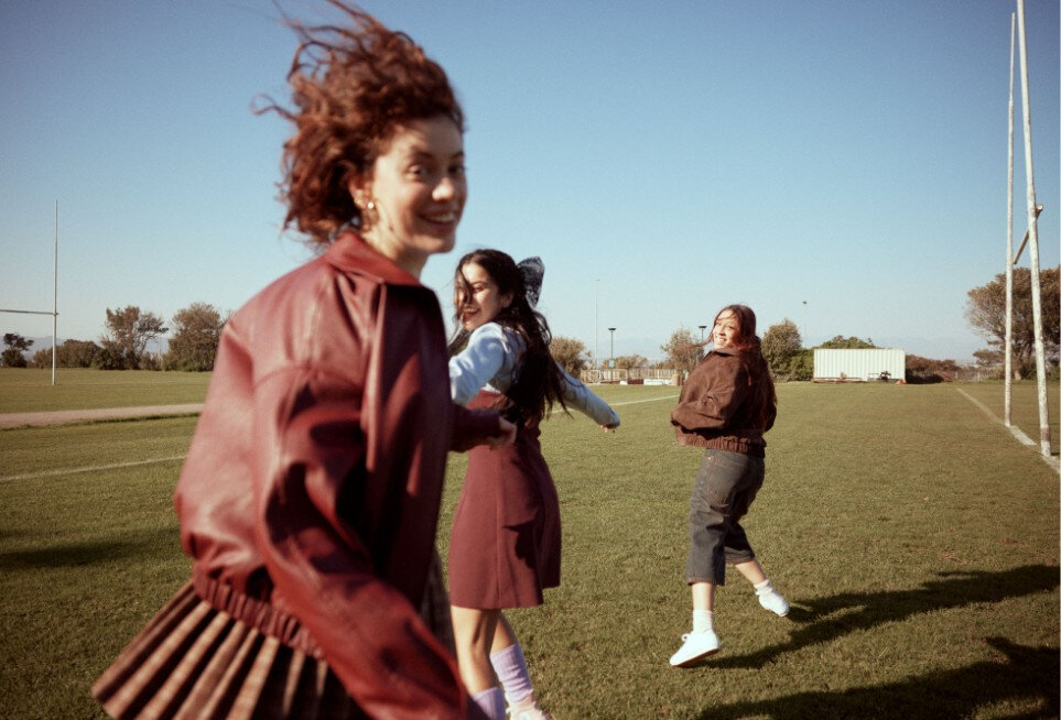 Smiling girls running in a grassy park, dressed in a schoolgirl-inspired style