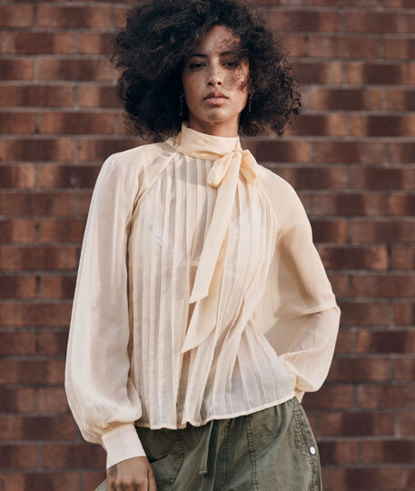 Femme debout portant une blouse crème avec col foulard