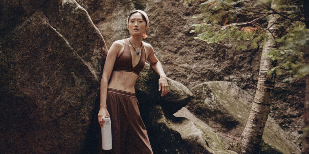 Woman leaning against rocks in a brown sports bra with matching joggers