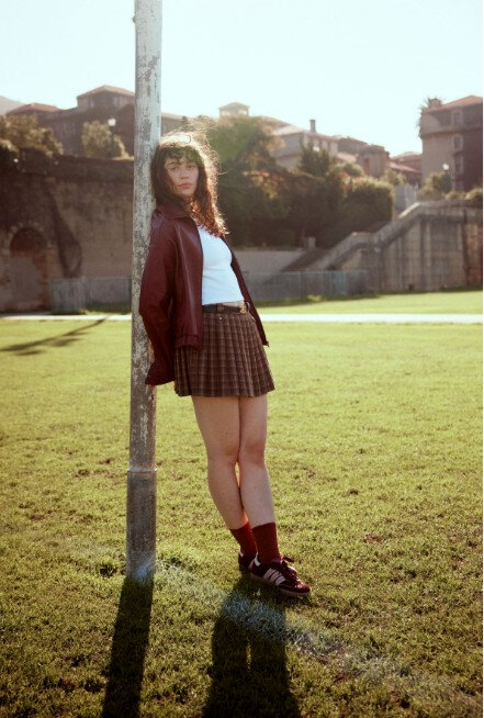 Young woman dressed in a schoolgirl-inspired outfit standing in a grassy park