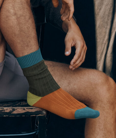 Gros plan sur un homme assis portant des chaussettes colorées à blocs vert, orange et bleu.