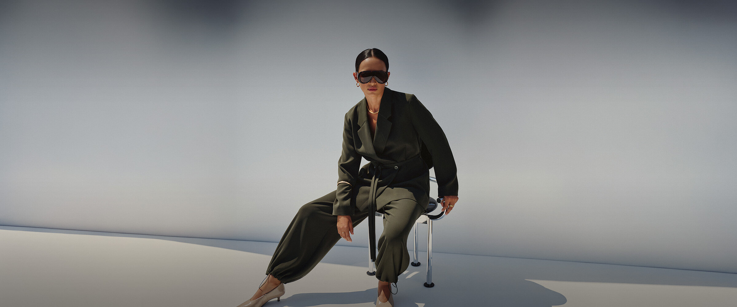 Femme portant un tailleur kaki avec de larges lunettes de soleil
