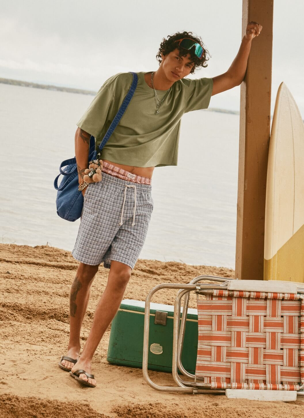 Jeune homme à la plage en t-shirt ample et court kaki et en short à carreaux