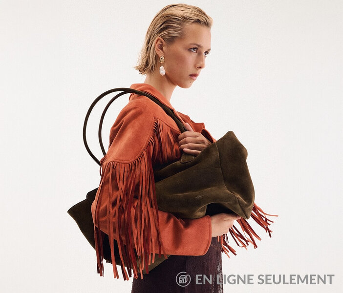 Jeune femme portant une veste en faux suède orange à franges et tenant un grand sac fourre-tout brun en faux suède