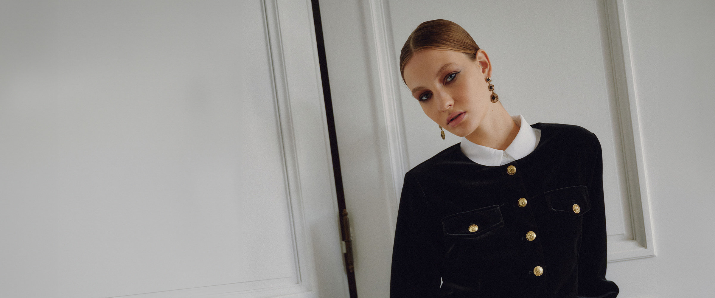Woman wearing a black velvet jacket with gold buttons.