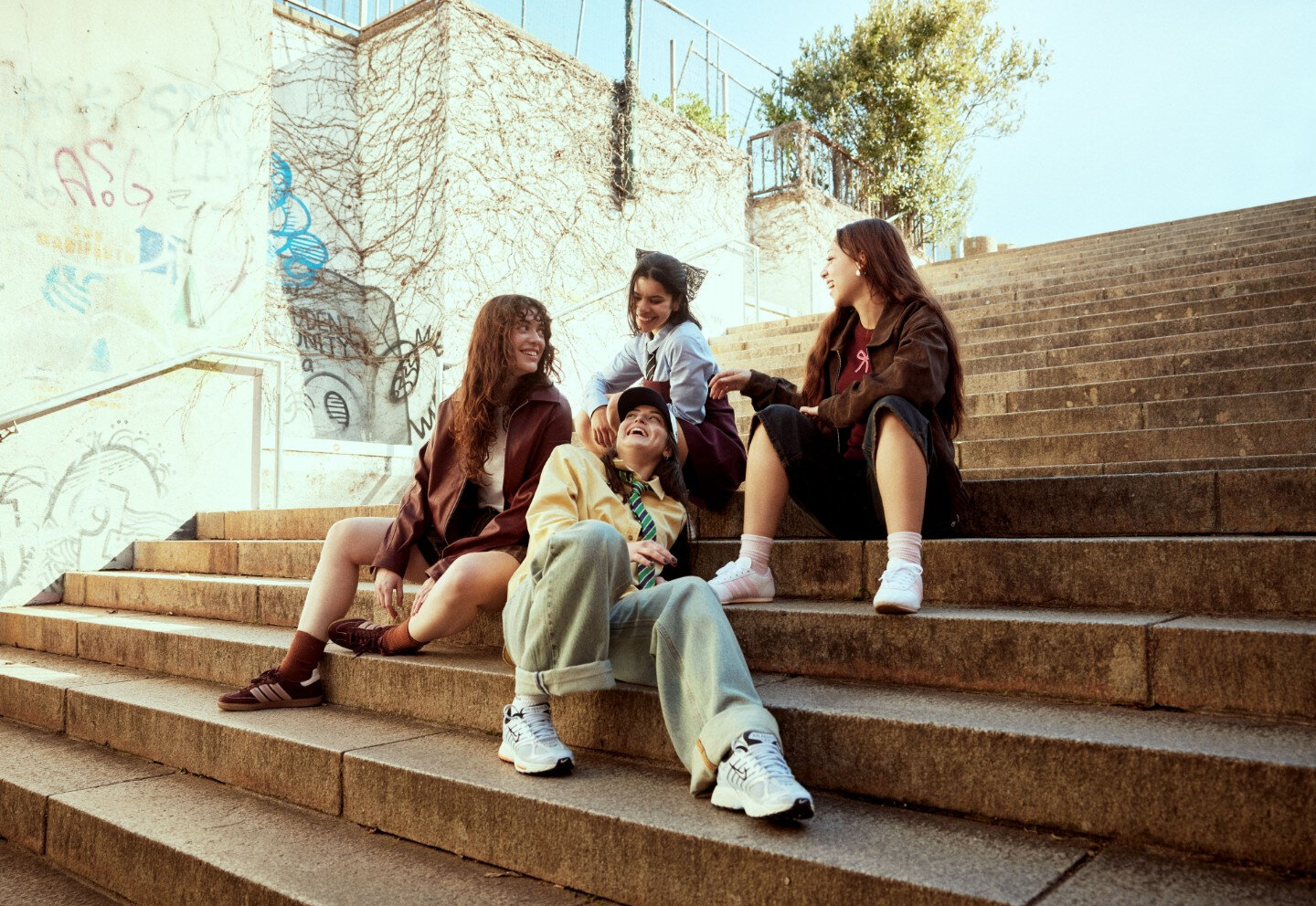 Jeunes filles riantes assises sur les marches d'un escalier public extérieur, vêtues dans un style d'inspiration écolière