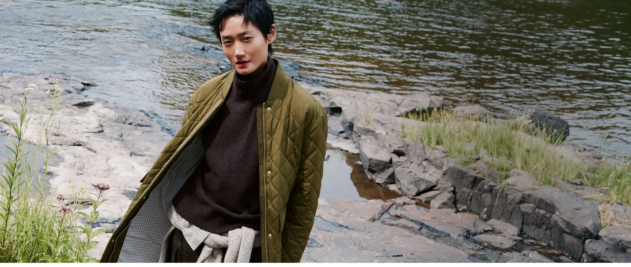 Femme au bord d'une rivière portant un long manteau matelassé vert, style bomber