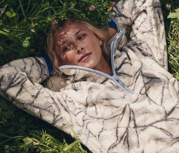 Une femme allongée dans l'herbe porte un haut en molleton moutonné crème à motifs foncés et à demi-fermeture éclair.