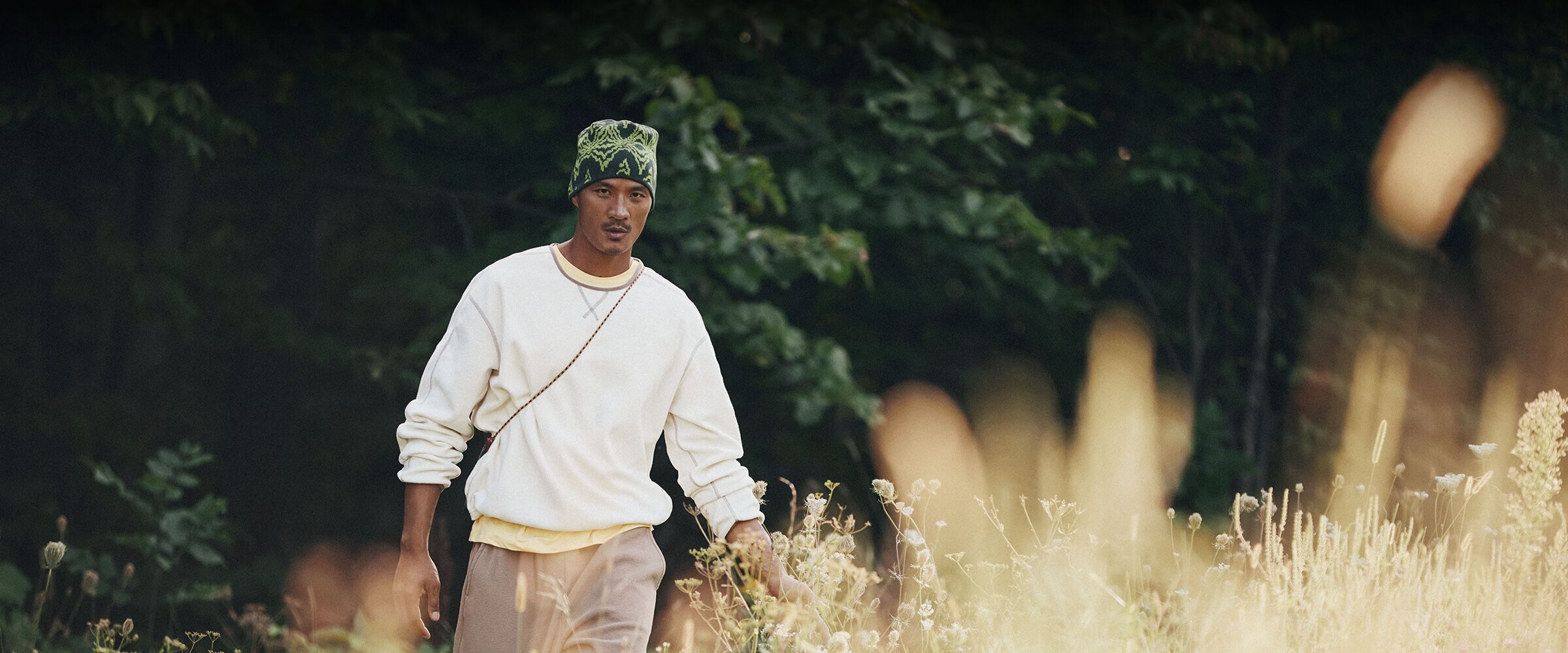 Man walking in a field, wearing a cream-colored sweatshirt.