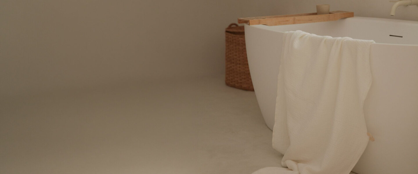 salle de bain beige avec un bain blanc, une serviette blanche et un plateau de bois.