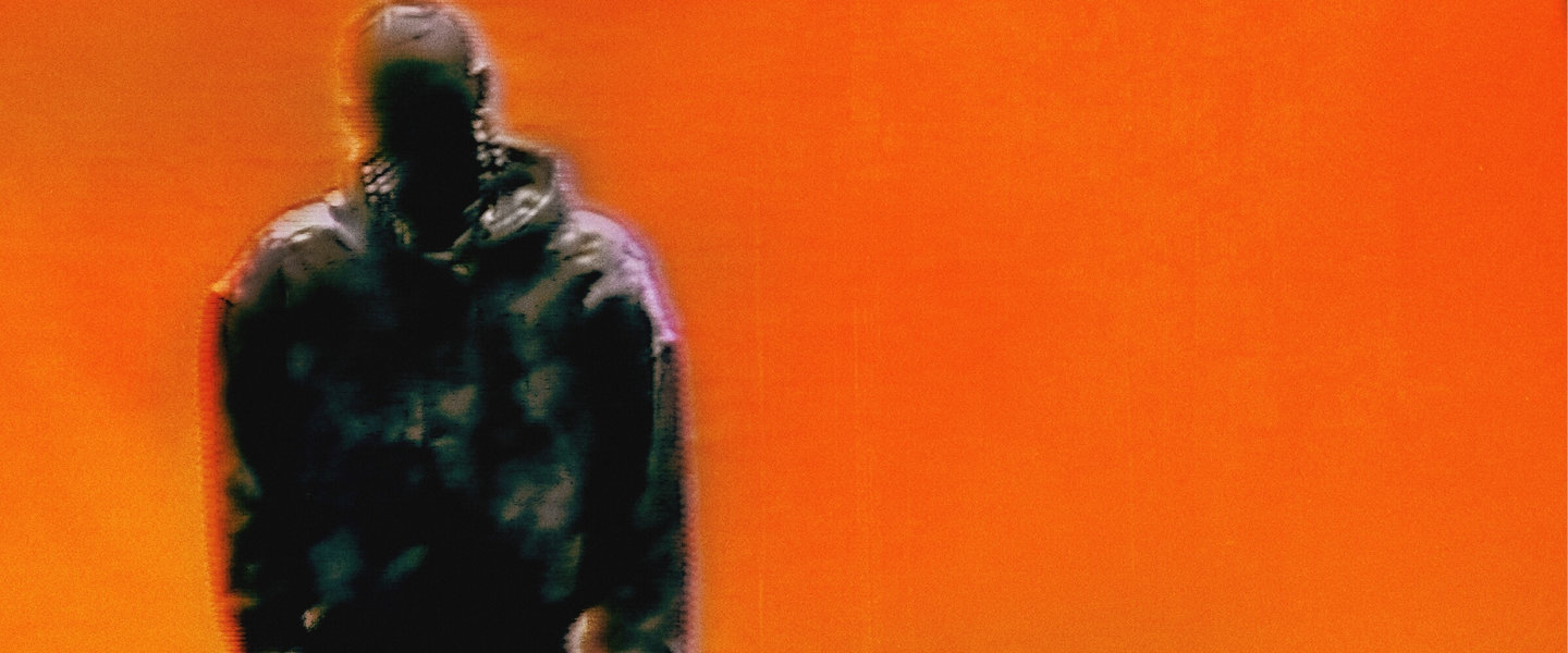 Blurred figure wearing a dark coat against a vivid orange background.