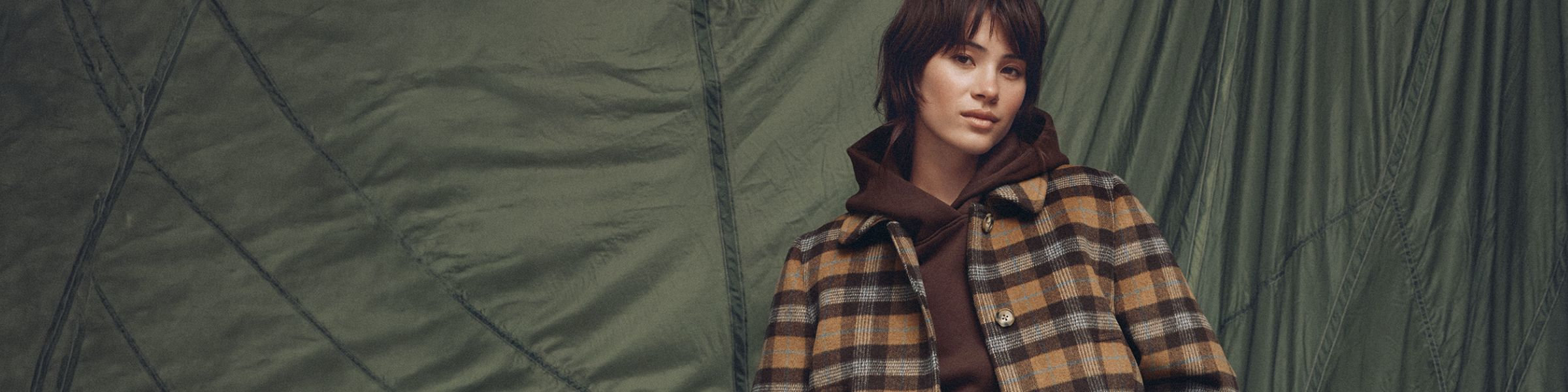 A young woman is wearing a brown hoodie under a plaid jacket