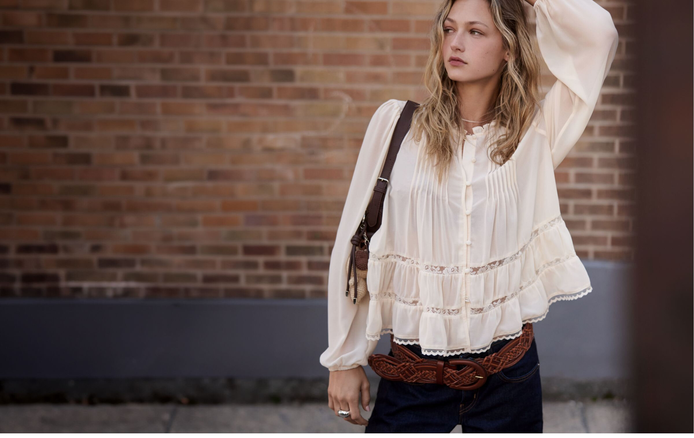 Photo of a young woman wearing a boho blouse in front of a brick wall