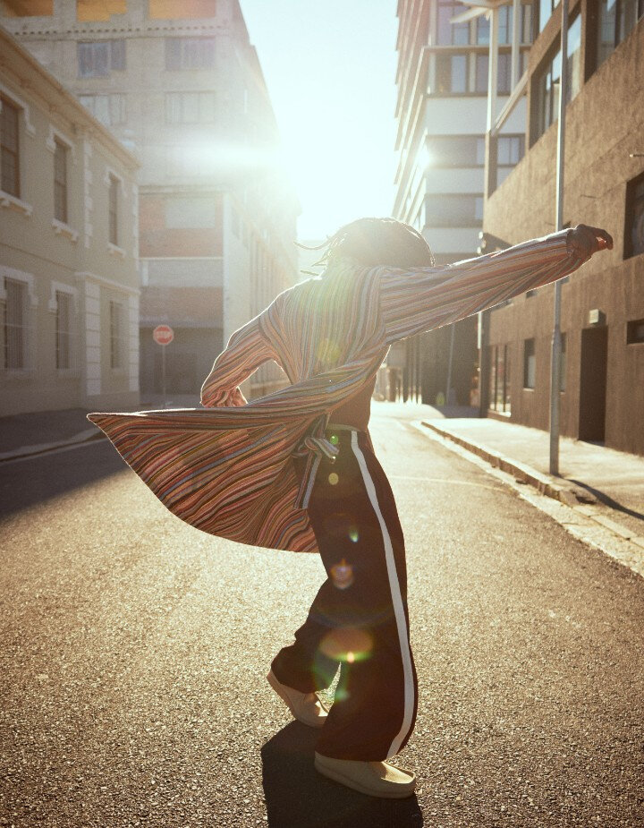 Homme qui danse vêtu d'un long peignoir ouvert à rayures multicolores et d'un pantalon sport noir avec une bande latérale blanche