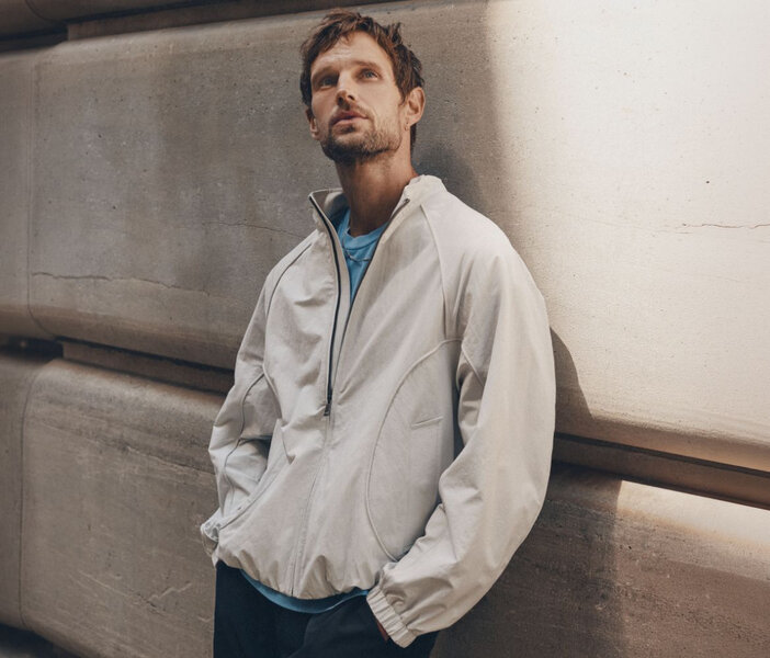 Un homme porte une veste coupe-vent grise à détails lisérés.