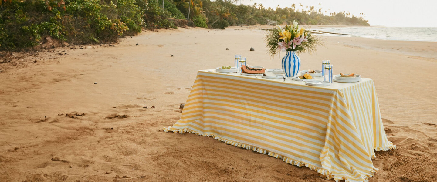 A table with various striped accessories on a beach in a paradise-like setting