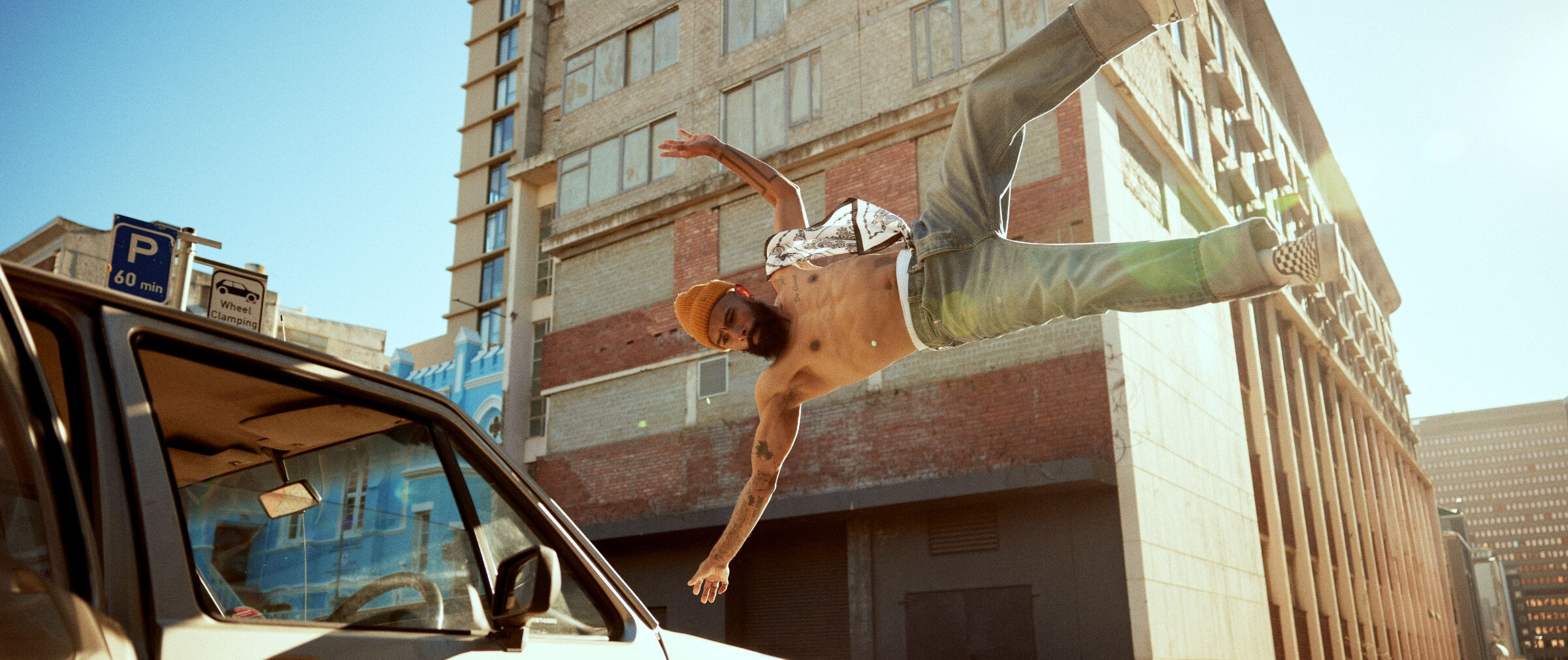 Shirtless man in jeans and an orange tuque in mid-air jump