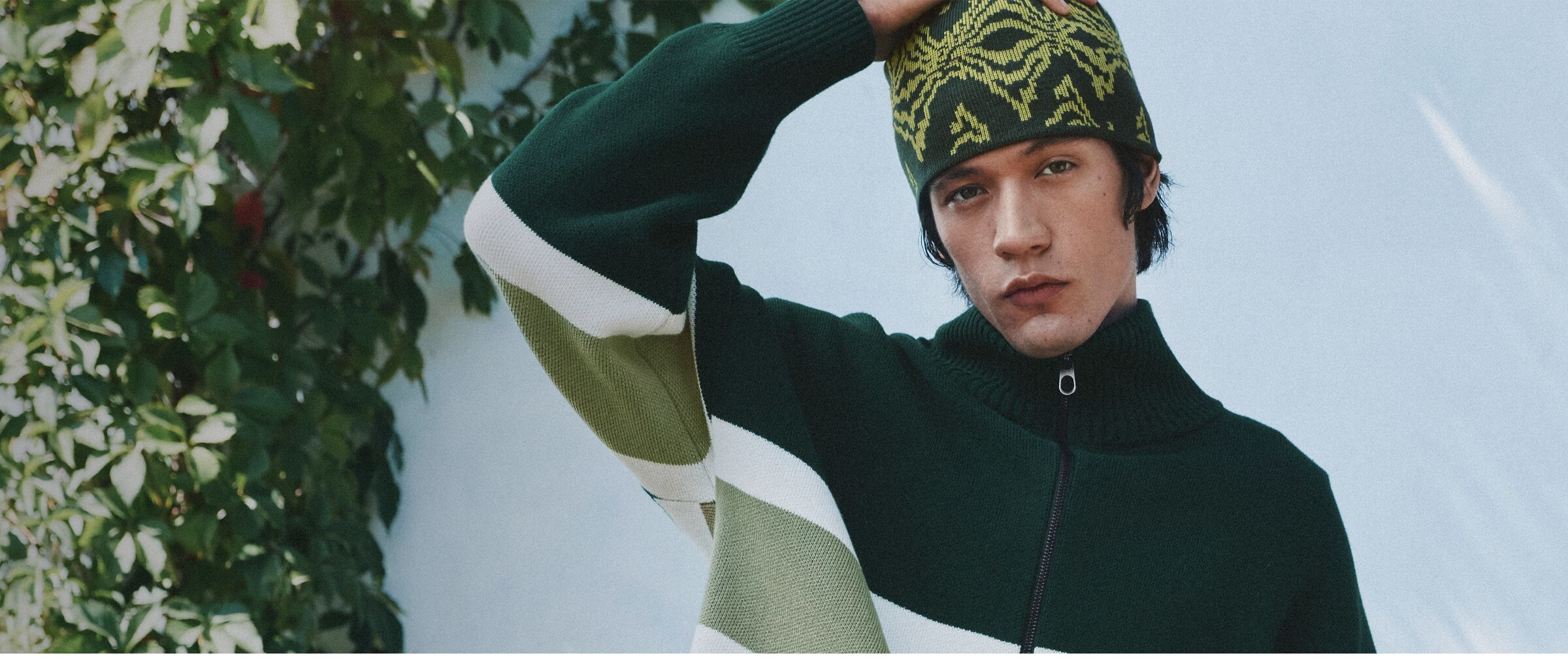 A young man is wearing a green large-stripes zipped sweater with a green patterned tuque