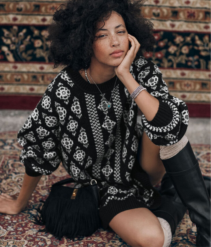 Seated woman wearing a black and white jacquard knit dress with folk-style patterns