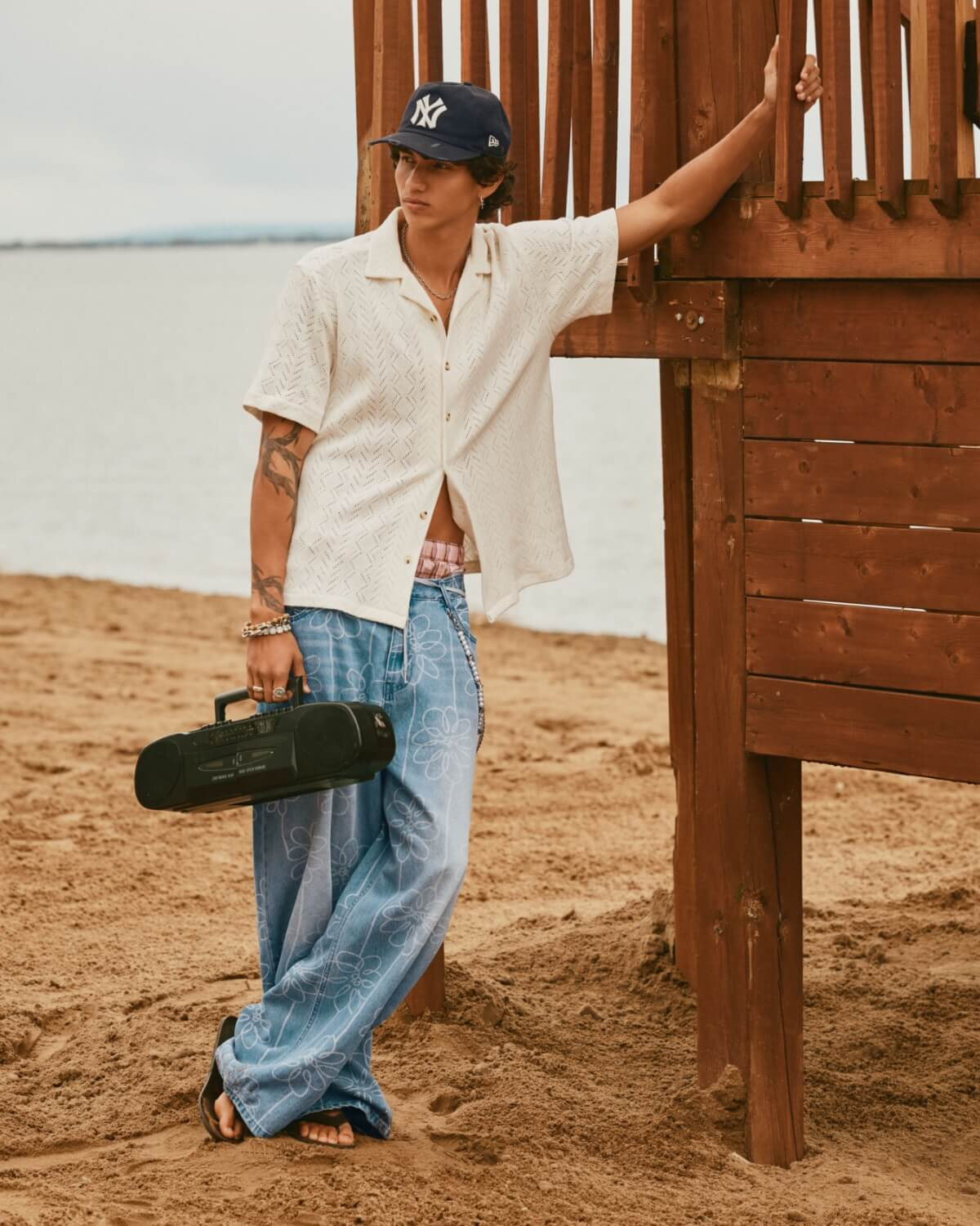 A young man at the beach wearing a cabana shirt and loose-fitting jeans