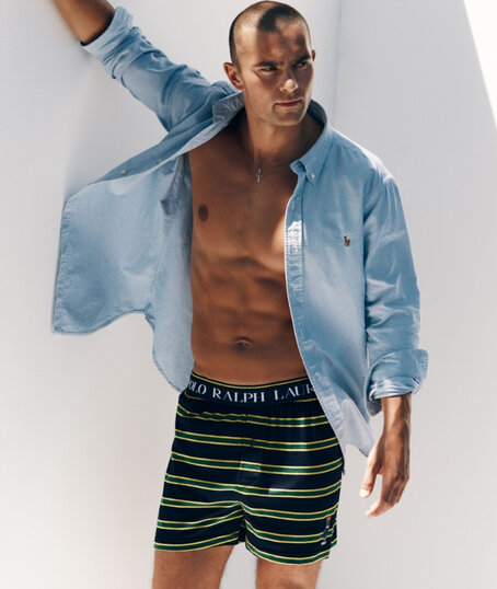 Homme portant une chemise bleu clair ouverte et un boxeur ample rayé noir, vert et jaune.