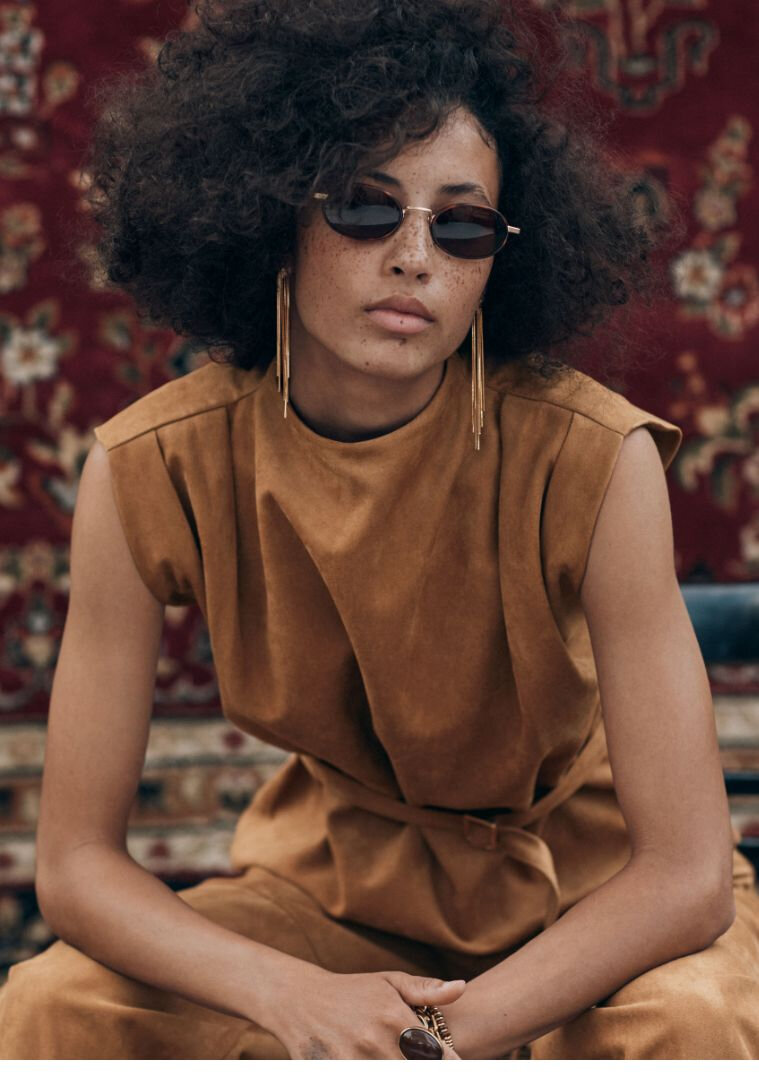 Femme portant une blouse ceinturée sans manche en faux suède et lunettes soleil