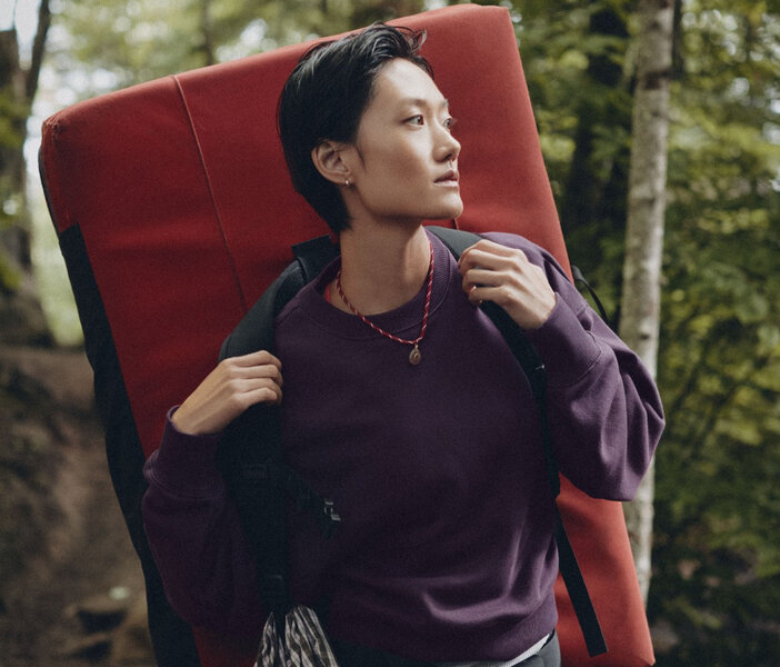 A woman is walking in nature wearing a deep purple long sleeve crewneck sweatshirt